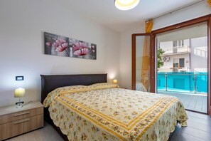 Une chambre à coucher avec un lit, des lampes de chevet, un tableau et un balcon donnant sur une piscine.