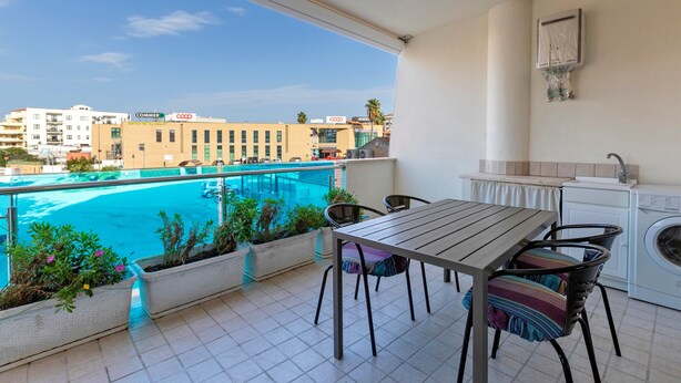 Ein Balkon mit Blick auf einen Pool, ein Tisch mit Stühlen, eine Waschmaschine und eine kleine Küchenzeile.