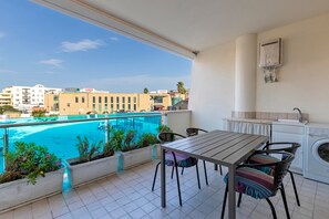 Un balcón con vista a la piscina, una mesa con sillas, lavadora y una pequeña cocina.