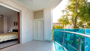 Ein Zimmer mit Bett, Kleiderschrank und einem Balkon mit Glasgeländer.