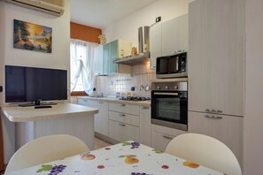 Una cucina compatta con schermo piatto, microonde, forno e tavolo da pranzo decorato con un motivo a frutta.