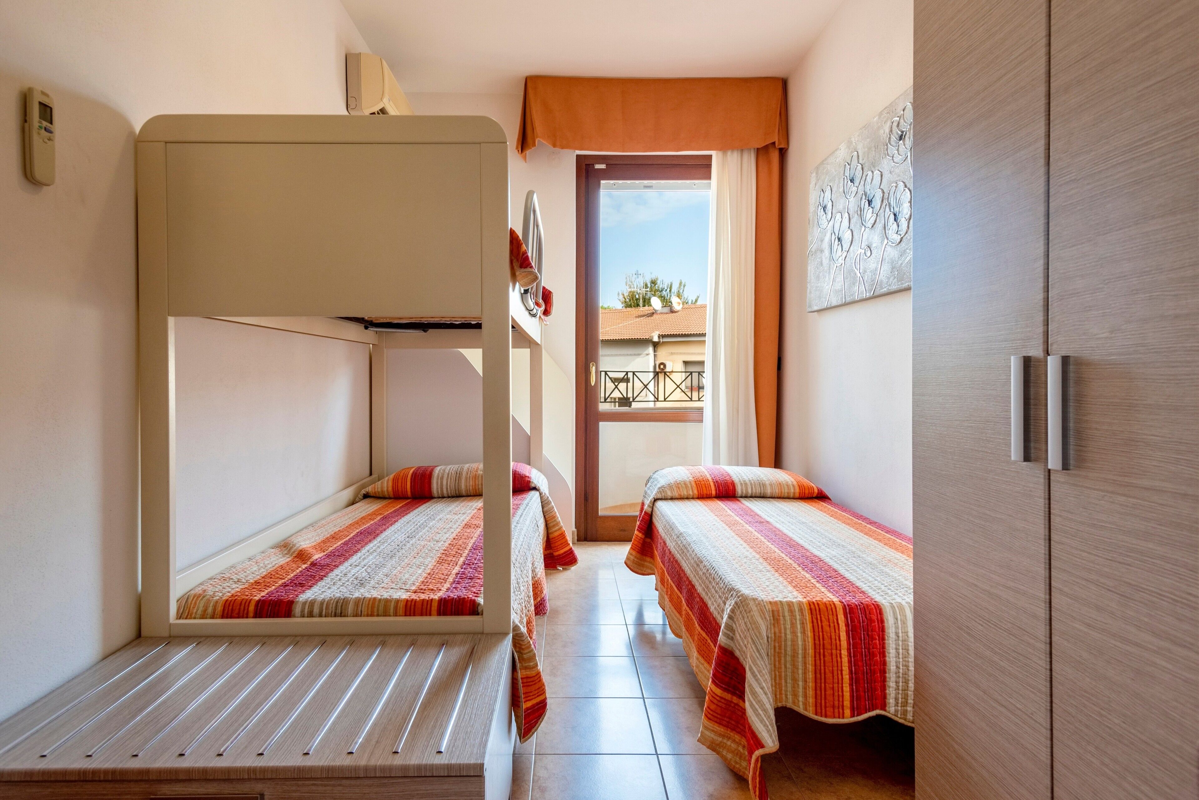 Ein Zimmer mit Etagenbetten, einer Tür, die auf einen Balkon führt, und einer Wandklimaanlage.