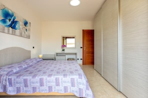 Une chambre à coucher comprenant un lit, une table de chevet, un miroir, une fenêtre et une armoire.
