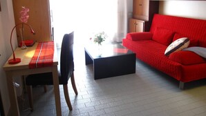 A room with a wooden desk, a red sofa, a black coffee table, and a chair. - Seaview flat with unforgettable terrace (Grado Pineta)