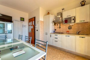 A modern kitchen with a microwave, stove, and cabinets. There is a dining table with chairs and a glass partition.