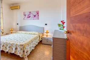 A bedroom with a bed, nightstands, a lamp, a wall-mounted air conditioner, and a door.