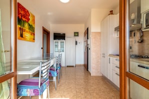 Un coin repas avec une table et des chaises en verre, une cuisine avec des meubles blancs et un tableau au mur.