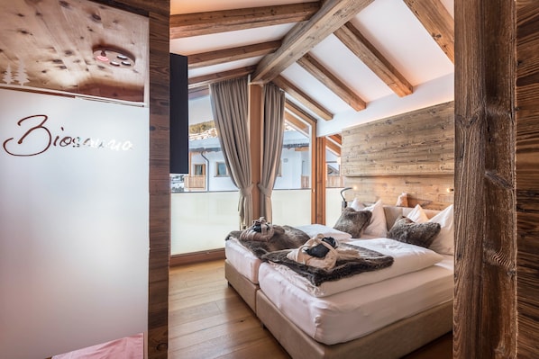 A bedroom with a wooden ceiling, a bed with a blanket, and a view of a building outside.