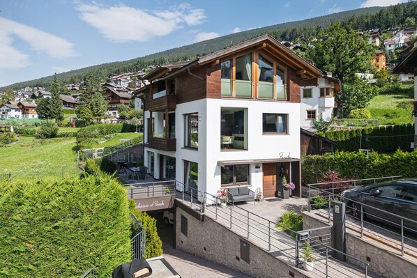 A multi-story house with a balcony, a garage, and a view of a green valley.