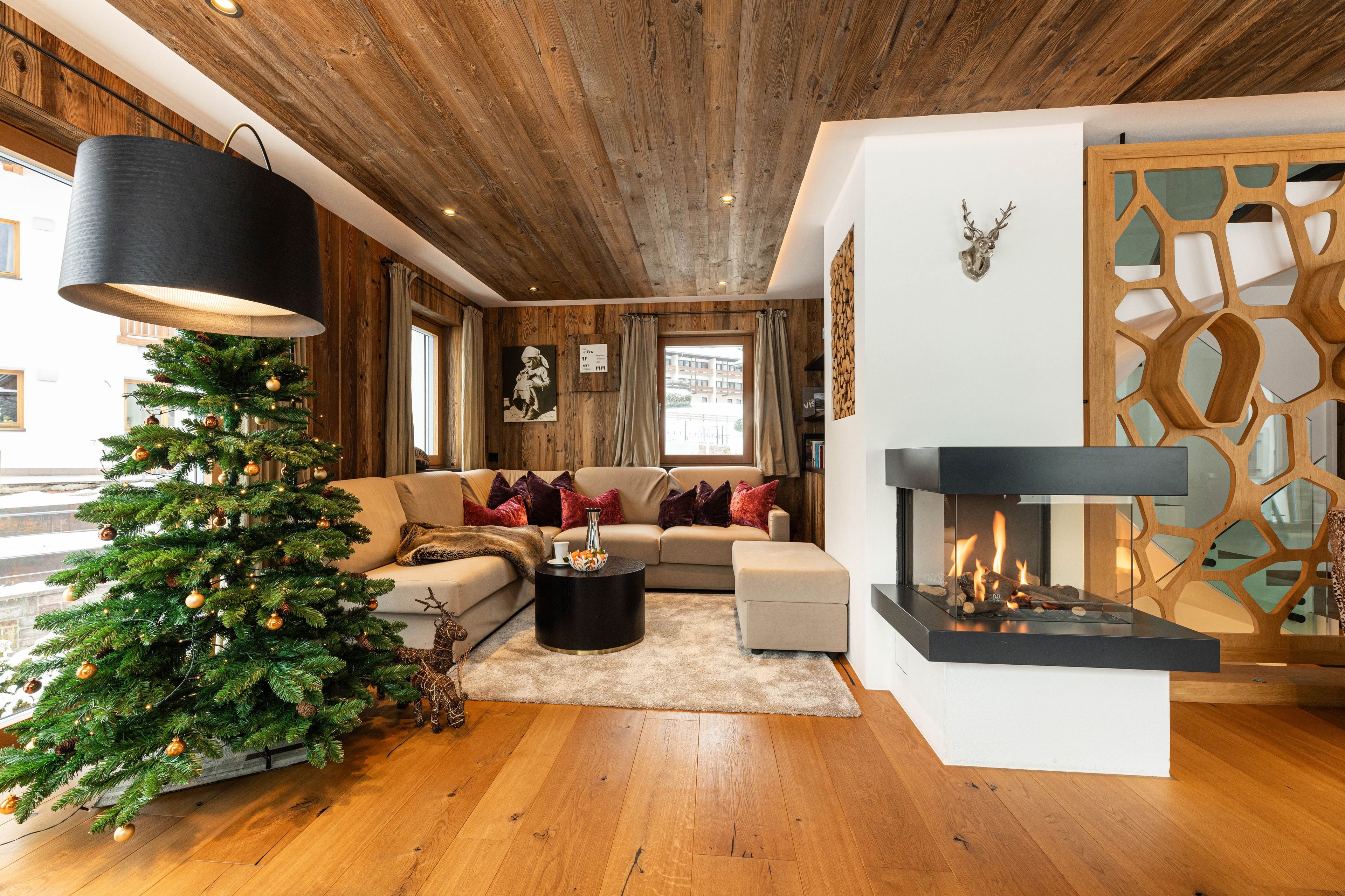 Ein gemütliches Wohnzimmer mit Holzbalkendecke, einem Weihnachtsbaum, einem Kamin und einer Couch mit Kissen.