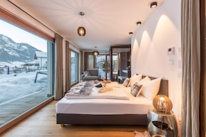 Ein modernes Schlafzimmer mit einem großen Bett, Blick auf eine verschneite Landschaft und Holzboden.