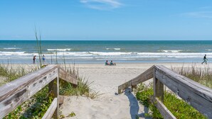 Une promenade en bois qui mène à une plage de sable où l’on peut admirer les vagues de l’océan.