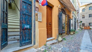 A narrow cobblestone street with buildings on either side, a wooden door with a sign, and a flag. - TOPAZ in OLD TOWN!  Romantic  near the sea! Alghero smart country style! Wi-Fi (Alghero)