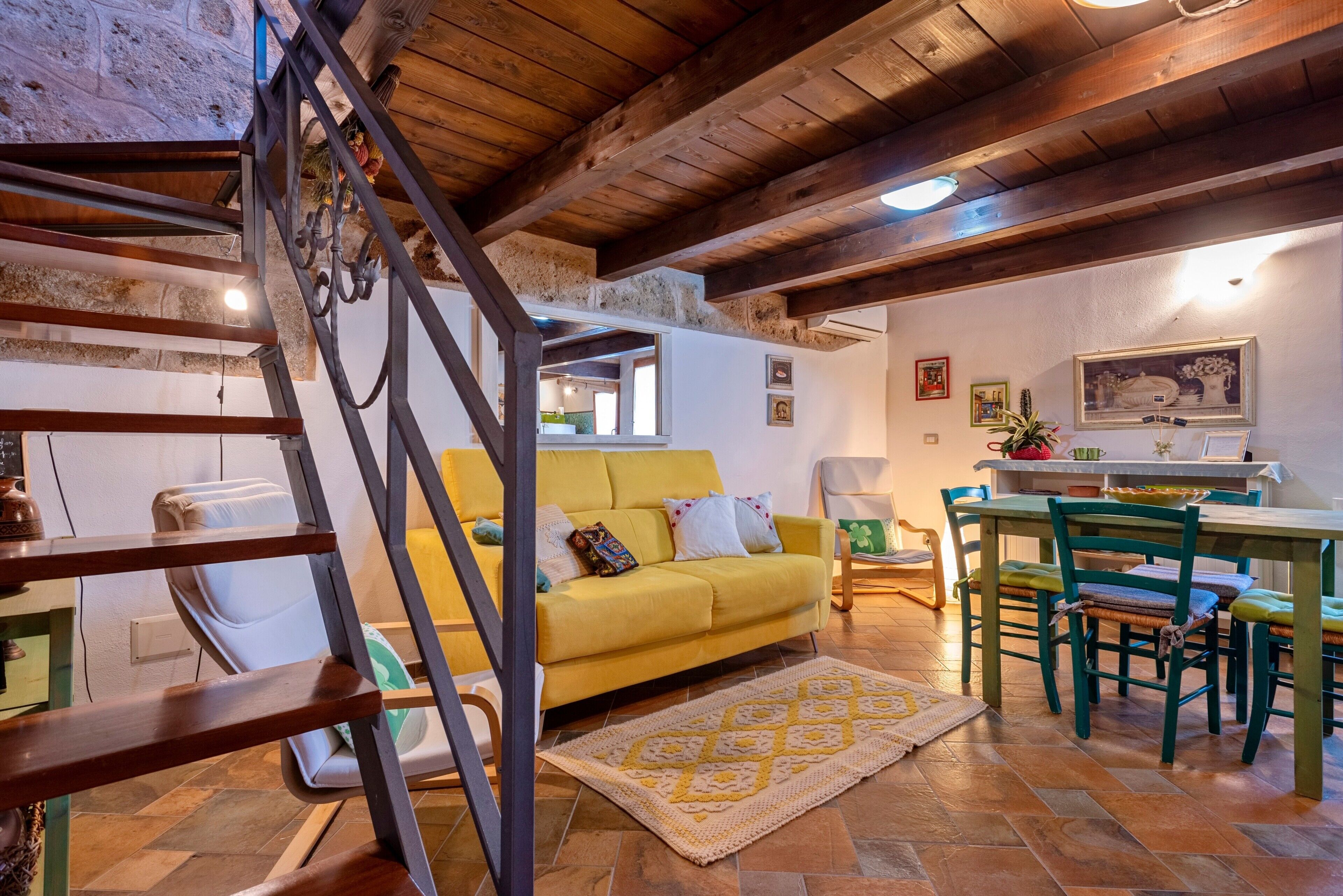 Un accogliente soggiorno con un divano giallo, una scala in legno e una sala da pranzo con sedie verdi.