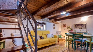 A cozy living room with a yellow sofa, a wooden staircase, and a dining area with green chairs. - TOPAZ in OLD TOWN!  Romantic  near the sea! Alghero smart country style! Wi-Fi (Alghero)