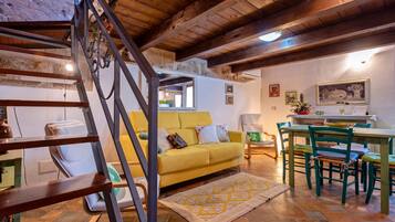 Un accogliente soggiorno con un divano giallo, una scala in legno e una sala da pranzo con sedie verdi.