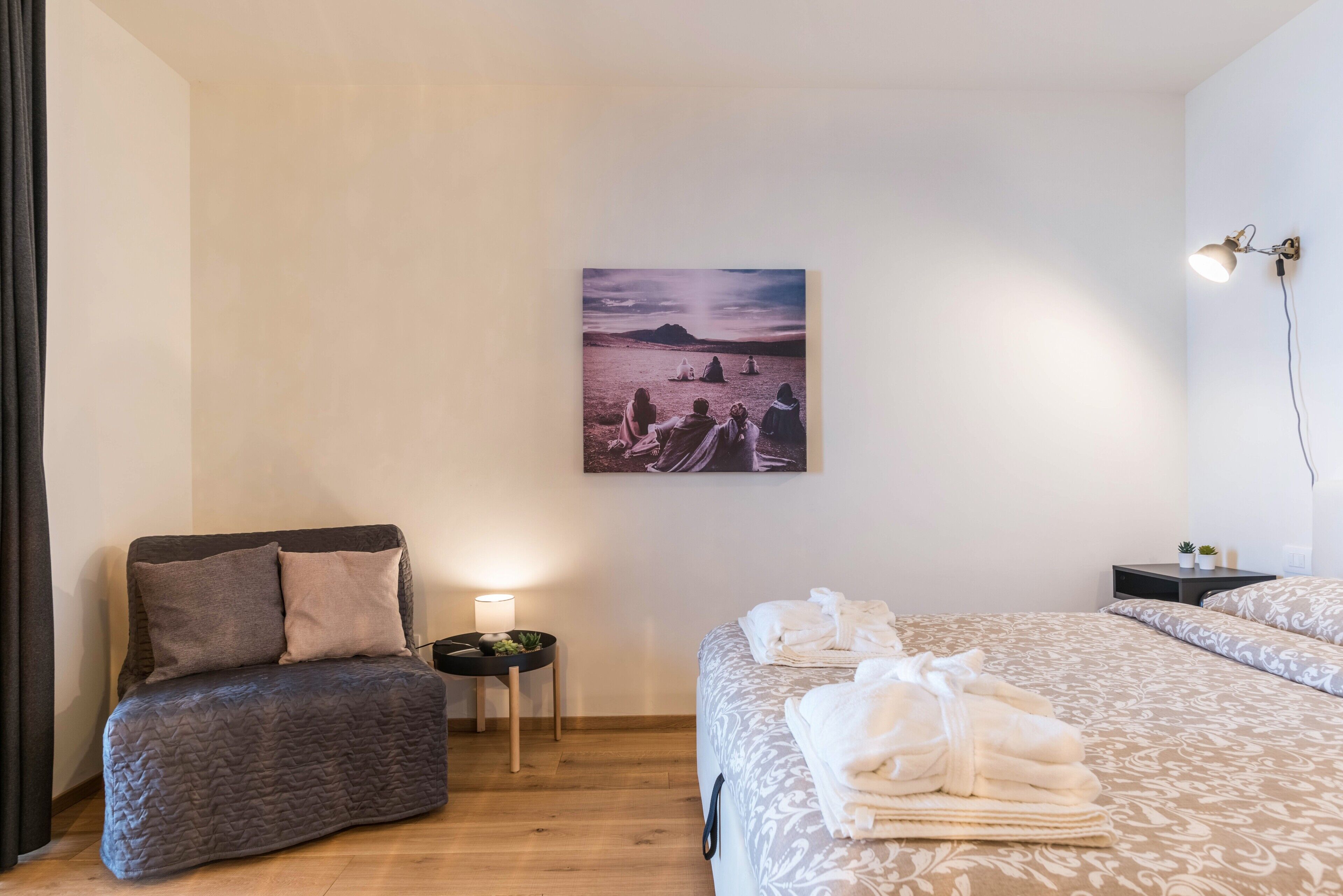 Ein Schlafzimmer mit Bett, Sessel, Nachttisch, Lampe und einem Bild an der Wand.