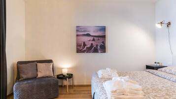 Ein Schlafzimmer mit Bett, Sessel, Nachttisch, Lampe und einem Bild an der Wand.
