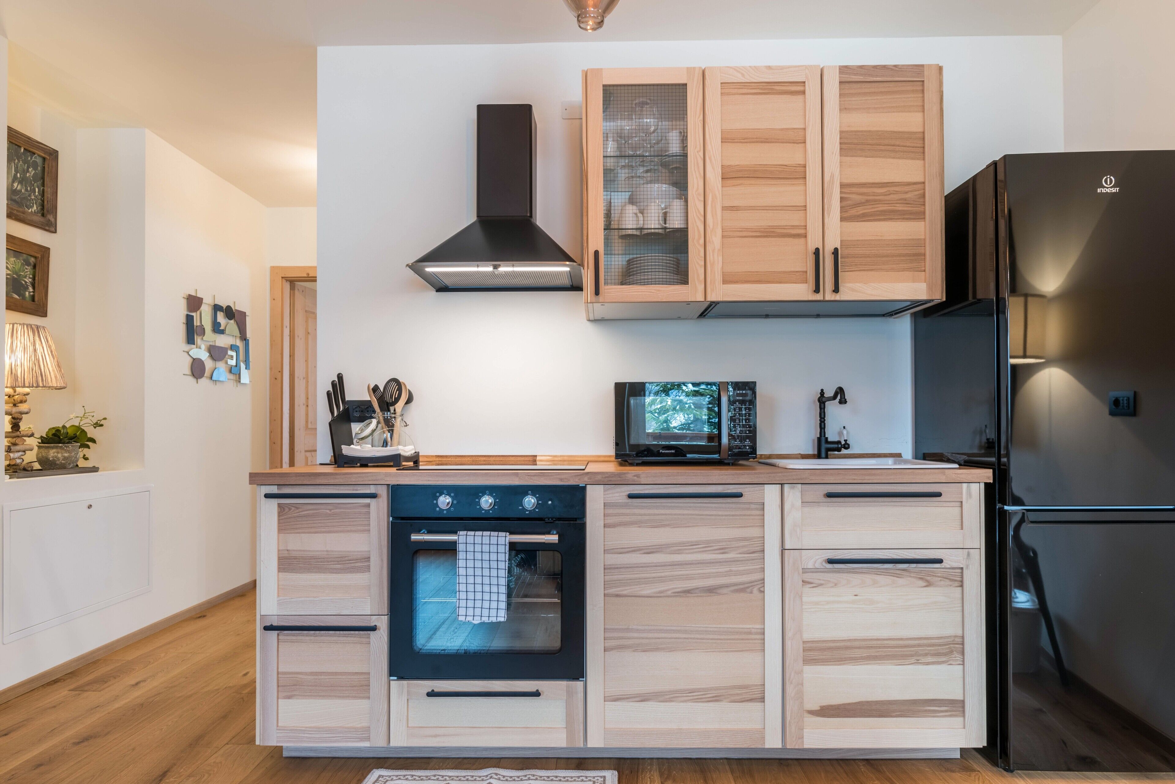 A modern kitchen with wooden cabinets, a built-in oven, a microwave, and a black refrigerator.