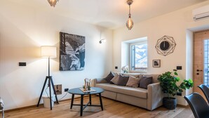 Ein Wohnzimmer mit einer Couch, einer Lampe, einem Tisch, einer Topfpflanze und einer Wanduhr.