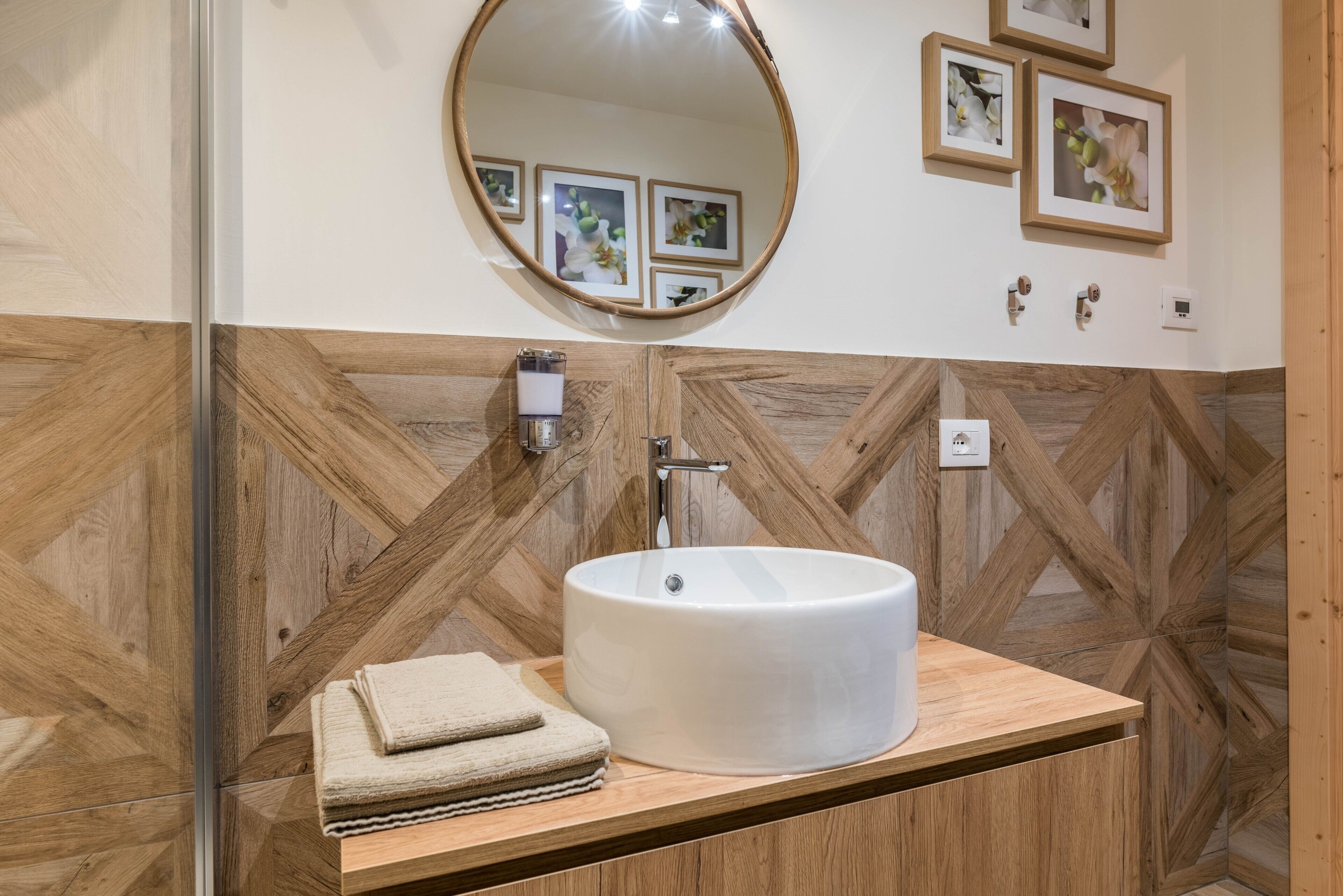 Une salle de bain avec un meuble-lavabo en bois, un lavabo rond, un miroir et des tableaux encadrés accrochés au mur.