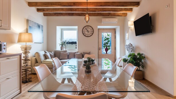 Un comedor moderno con una mesa de vidrio, sillas blancas, techo de madera y un televisor montado en la pared.