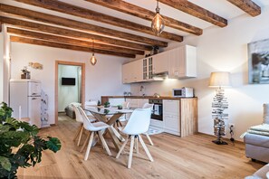 A modern kitchen with wooden beams, white cabinets, a dining table with chairs, and a floor lamp.