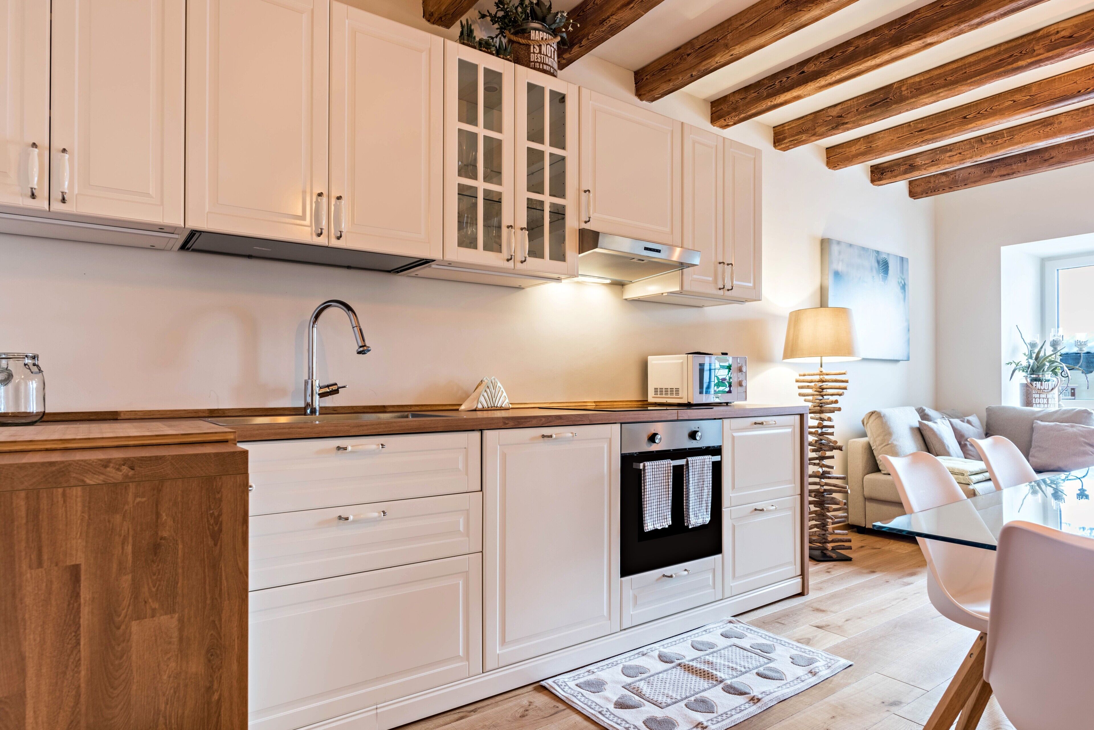 A modern kitchen with white cabinets, a wooden countertop, a built-in oven, and a dining area with a glass table and chairs.
