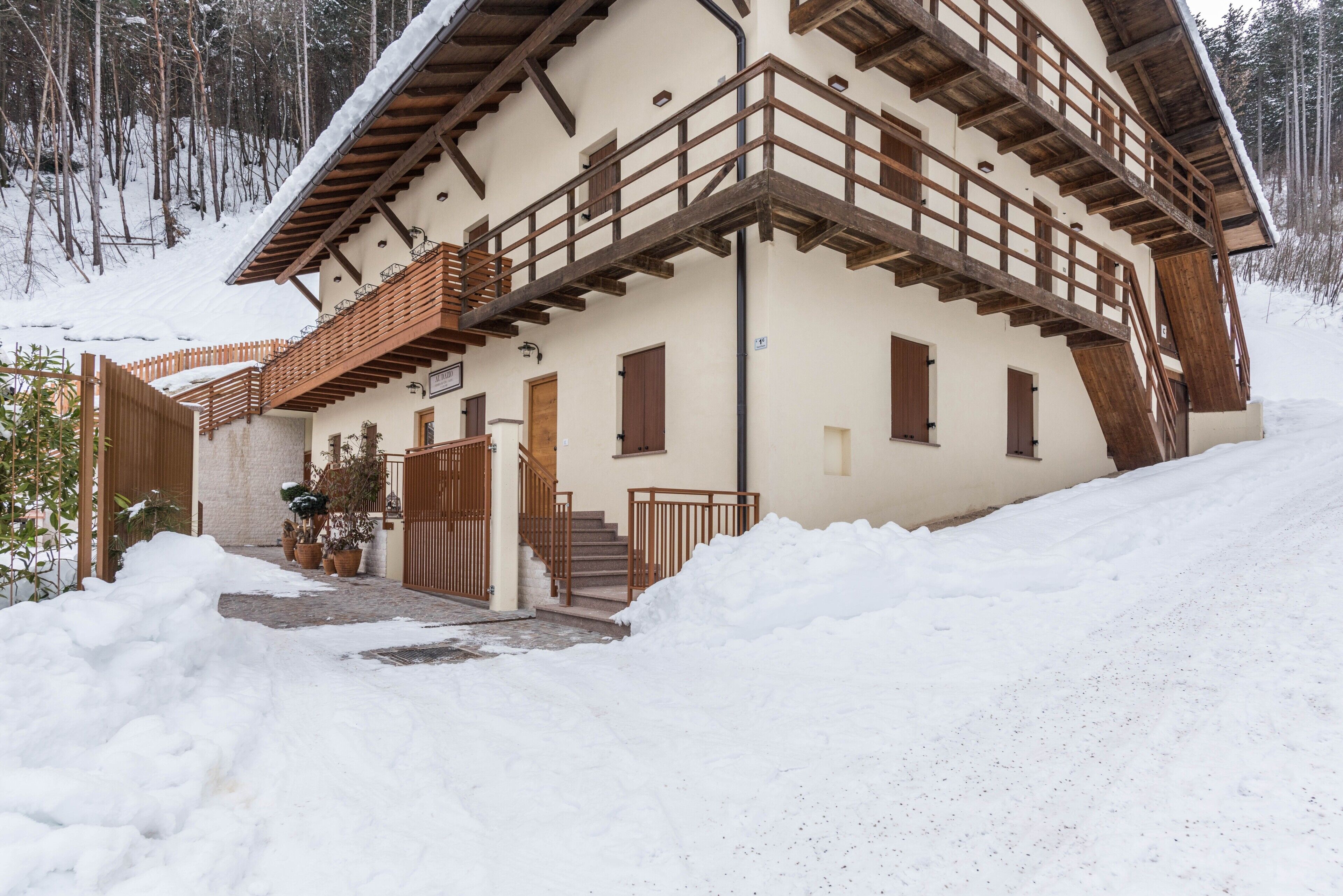 Eine zweistöckige Chalet mit Holzbalkon, einer Treppe und einem verschneiten Eingang.