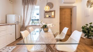 Une cuisine moderne avec des meubles blancs, une table à manger en verre et un plafond en bois.
