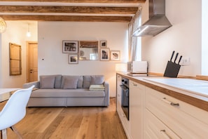 Una sala de estar acogedora con un sofá, una zona de comedor con una silla, una cocina con estufa y vigas de madera en el techo.