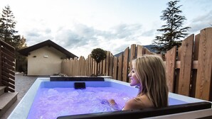 Une personne dans un bain à remous, avec une clôture en bois et un bâtiment en arrière-plan.