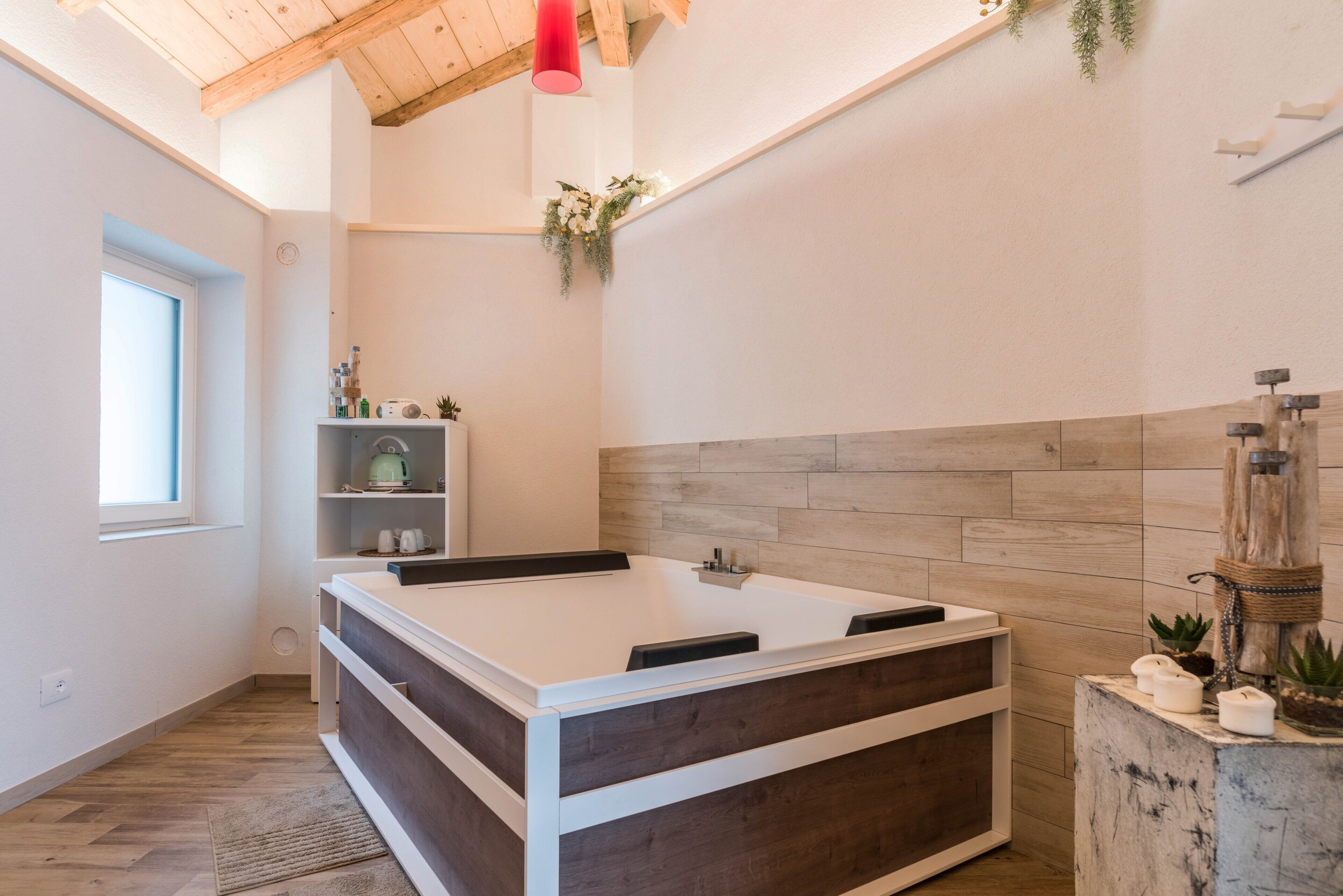 A modern bathroom with a freestanding bathtub, wooden flooring, a white vanity, and a window.