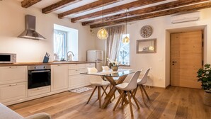Une cuisine moderne avec des poutres en bois, un îlot central, des meubles blancs et des luminaires suspendus.