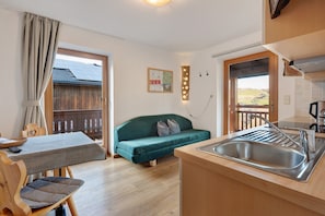 A compact kitchen with a sink, wooden cabinets, and a green sofa.
