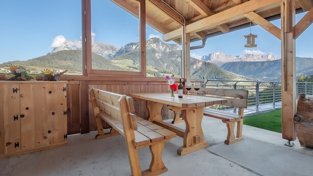 A wooden outdoor seating area with benches and a table, overlooking a mountainous landscape. - Schlern – Authentic Farm Stay with Animals, Sauna & Mountain Views (Collepietra)