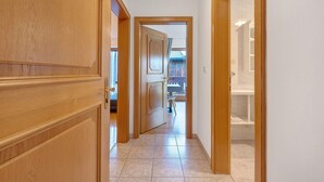 A hallway with wooden doors and a tiled floor leading to a bathroom with a shower and a toilet. - Schlern – Authentic Farm Stay with Animals, Sauna & Mountain Views (Collepietra)