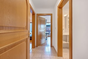 A hallway with wooden doors and a tiled floor leading to a bathroom with a shower and a toilet.