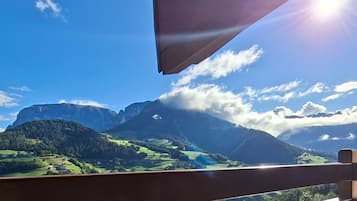 A balcony with a view of mountains, a table with two mugs, and a coffee pot.