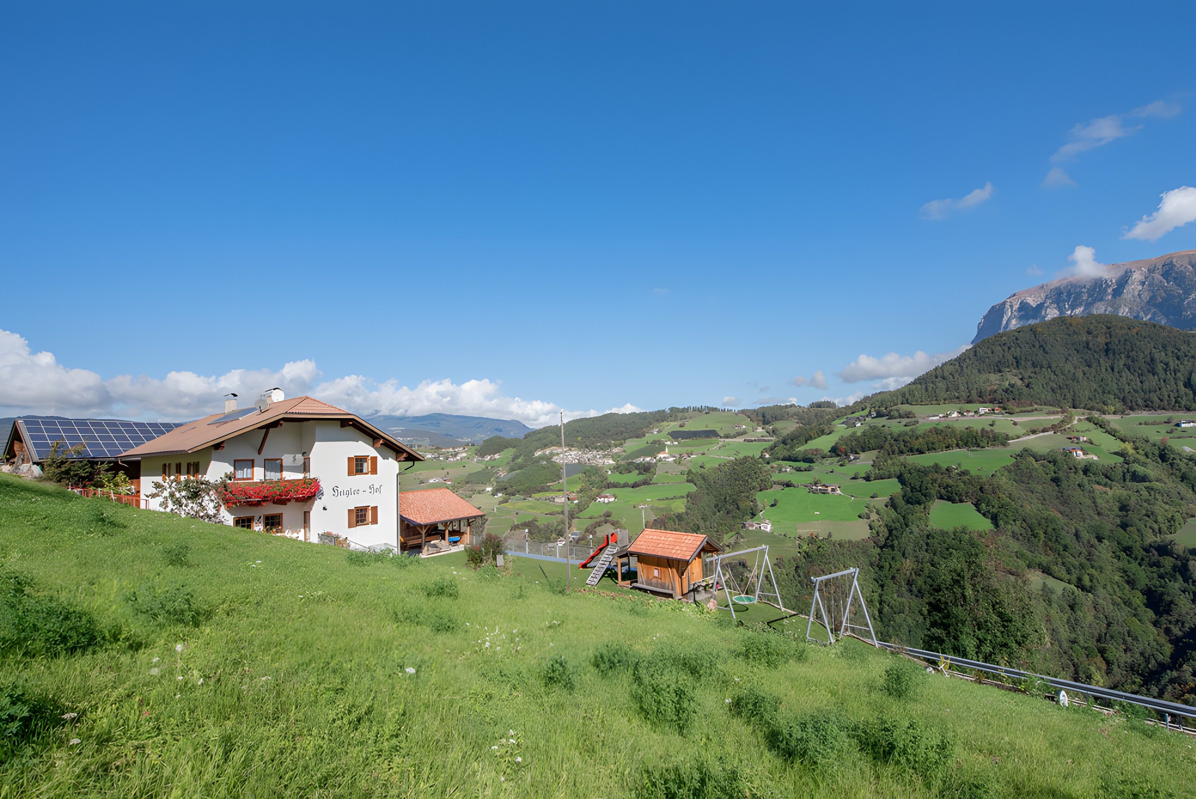 A house with a red roof, solar panels, and a view of a green valley.