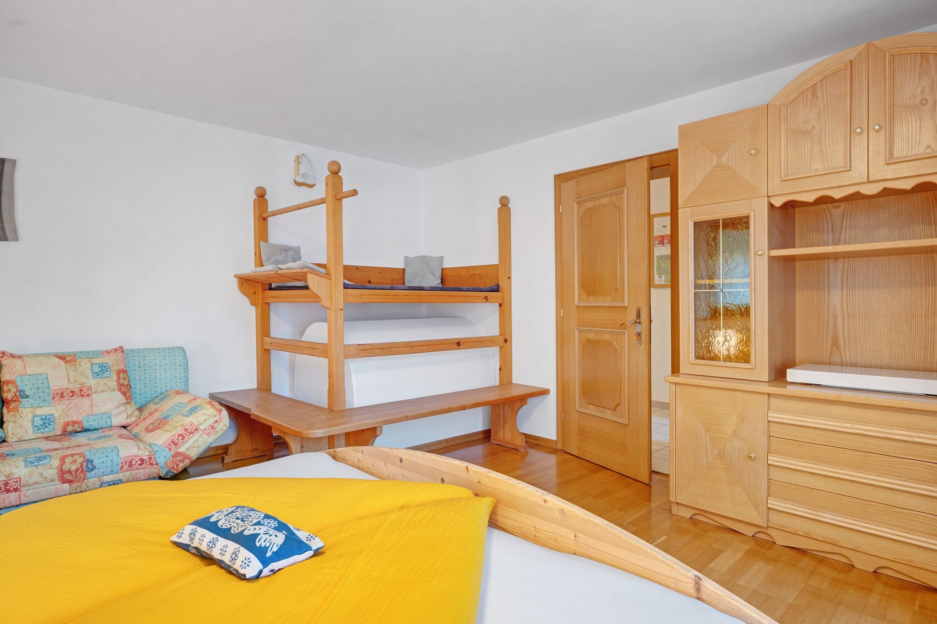 Une chambre avec un lit superposé, une armoire en bois et un canapé agrémenté de coussins à motifs.