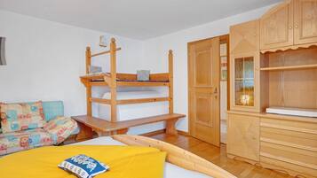 Une chambre avec un lit superposé, une armoire en bois et un canapé agrémenté de coussins à motifs.
