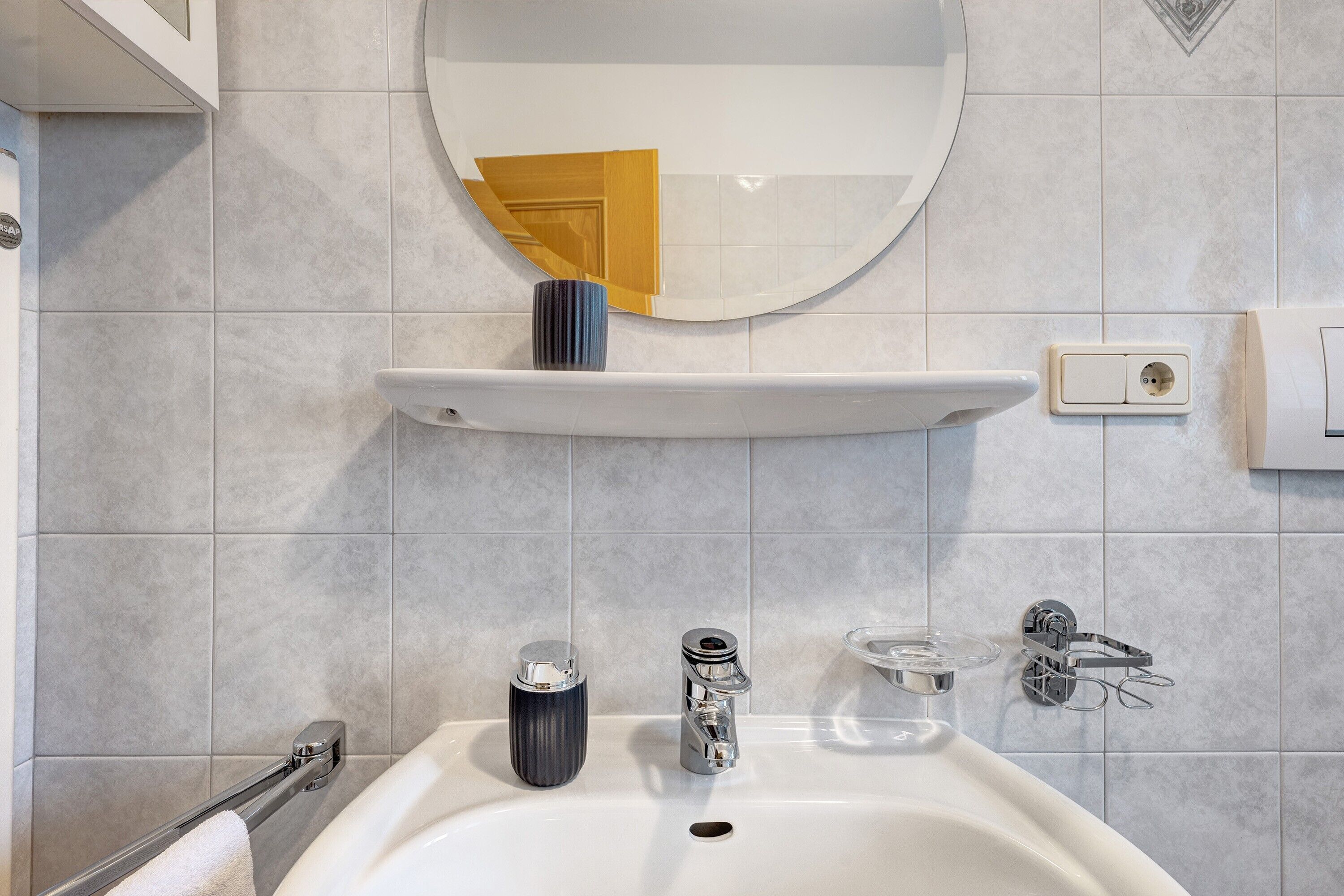 Une salle de bain avec un lavabo blanc, un miroir, un porte-serviettes, un porte-savon et une serviette.