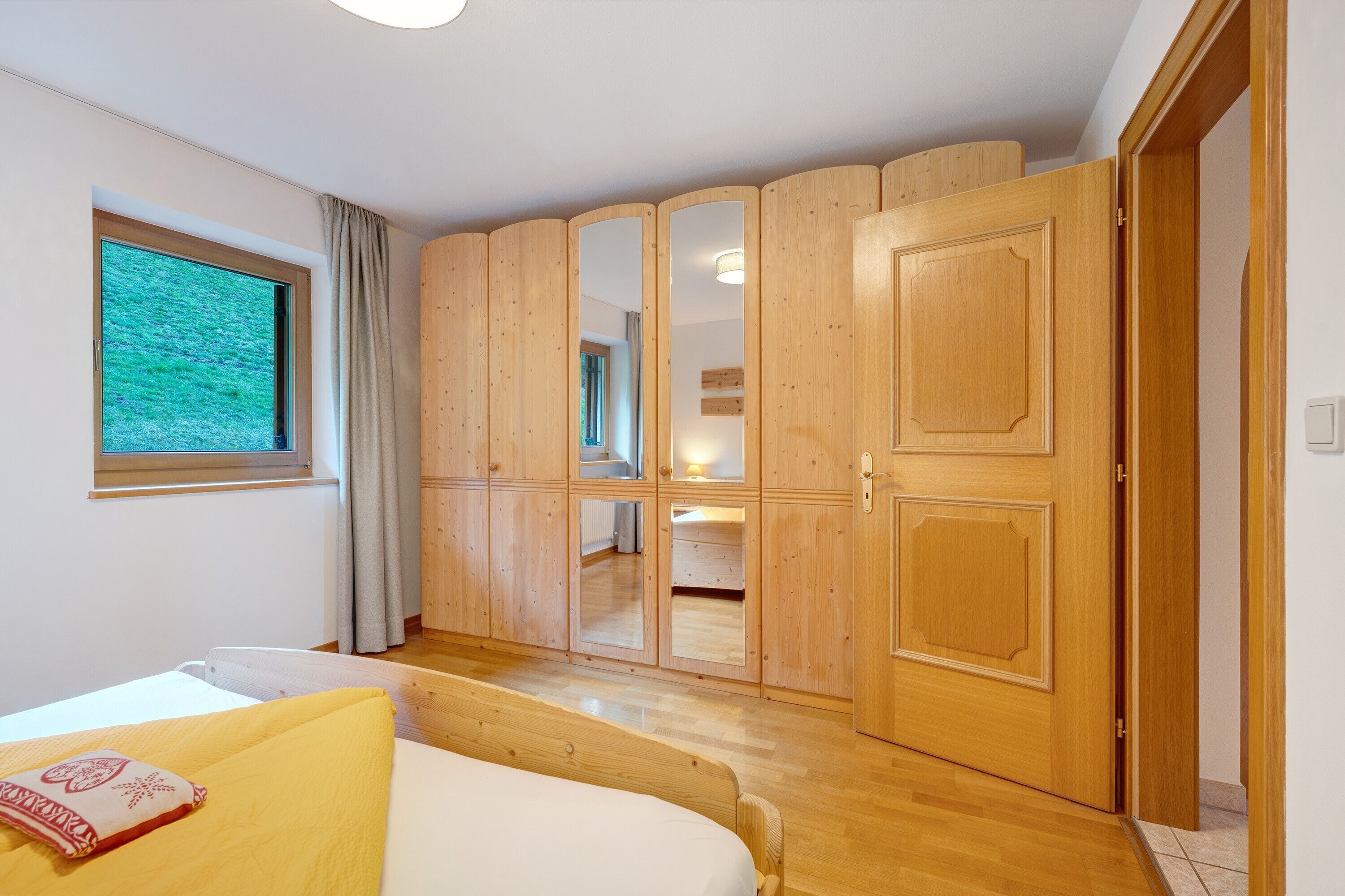 A bedroom with a bed, wooden wardrobe, and a window.