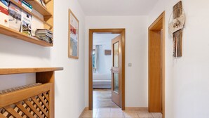 Un couloir avec une porte en bois, une étagère fixée au mur où sont posés des magazines, et un objet décoratif.