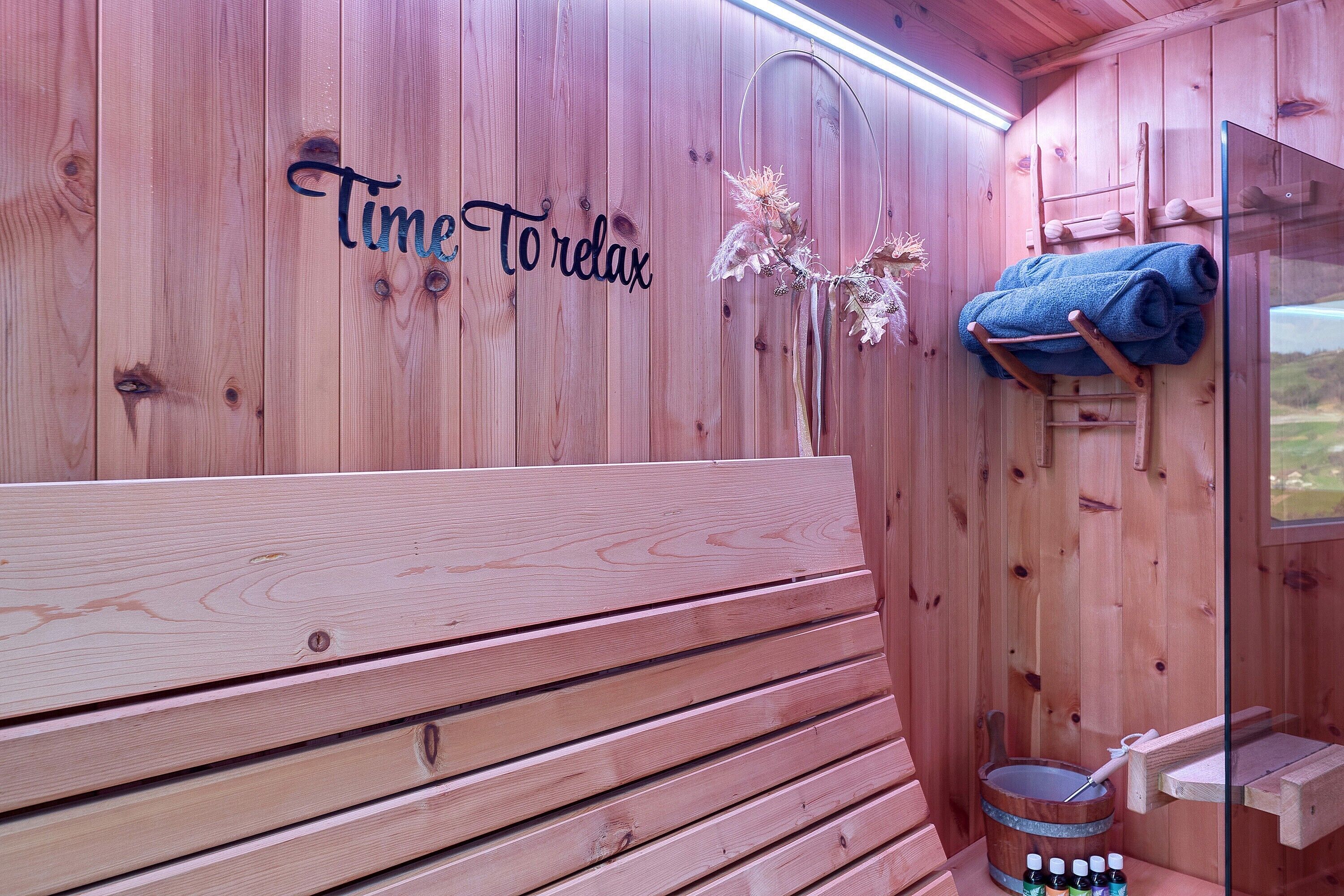 A wooden sauna with a bench, a towel rack, and a bucket with bottles.