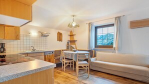 Une cuisine avec des meubles en bois, une table à manger avec des chaises, un four encastré et une fenêtre avec des rideaux.