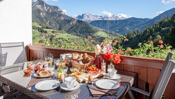 Une table dressée pour le petit-déjeuner, avec vue sur la montagne, comprenant un panier en osier avec du pain et un pot de confiture.