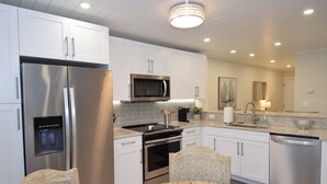 A modern kitchen with white cabinetry, stainless steel appliances, and a dining area with a wooden table and chairs. - Stay at the Best Condo in the Complex, 5 floor with privacy and best water view! (Marco Island)