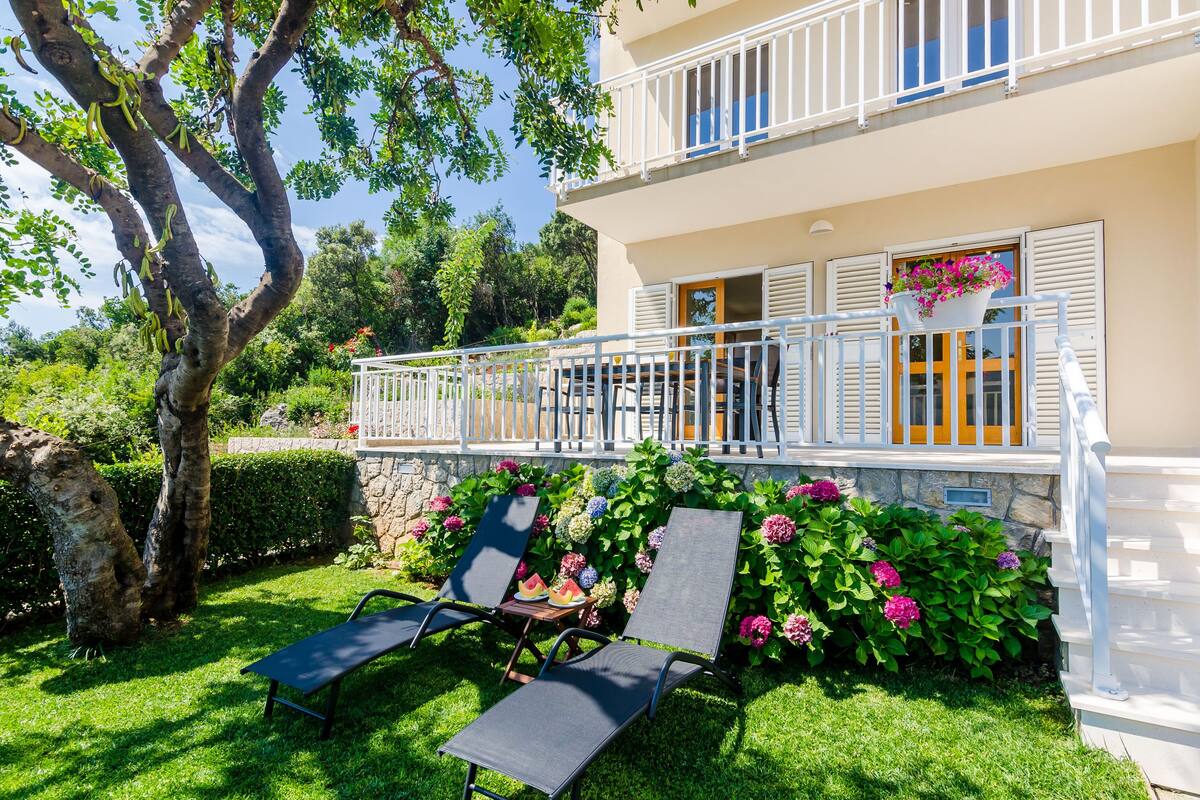 A two-story building with a balcony, outdoor seating, and lush greenery.